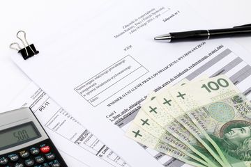 Leżące luźno na stole przedmioty: długopis, kalkulator, formularz wniosku i pięć banknotów stuzłotowych.