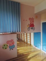 OsrodekJPII remont 10 Fragment sali do rehabilitacji. Parkiet, niebieski drzwi. Obok niebieskiej żaluzji na ścianie rysunki z bajki Świnka Pepa