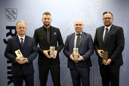 Czterech mężczyzn w ciemnych garniturach. Wszyscy trzymają w rękach statuetki. 