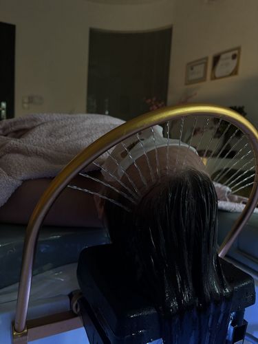 Zdjęcie przedstawia leżącą kobietę, która jest w trakcie kąpieli głowy w salonie SPA.