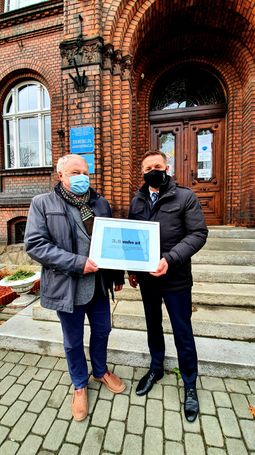 Prezydent Rybnika Piotr Kuczera oraz prof. nadzw. dr hab. inż. Joachim Foltys z symbolicznym czekiem na 3,5 mln złotych dla szpitala przed ceglanym budynkiem szpitala psychiatrycznego