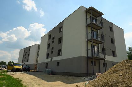 Jasne, kilkupiętrowe budynki mieszkalne z balkonami na tle błękitnego nieba z chmurami.