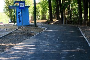 Asfaltowa droga rowerowa biegnąca wzdłuż ulicy, przystanek, po obu stronach drogi las
