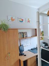 OsrodekJPII remont 11 Gabinet - meble biurowe,na biurku monitor i drukarka, na szafie kwiatek w doniczce. Na białej ścianie 3 prace dzieci w antyramach.