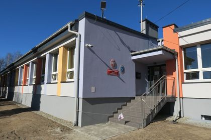 Piętrowy budynek szkoły po remoncie. Wokół niezagospodarowany teren zielony.