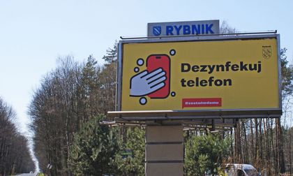 Bilbord cov1 3 Bilbord na tle błękitnego nieba i kron drzew.