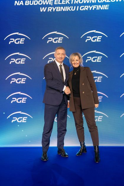 Mężczyzna i kobieta stojący przed ścianką. Ściskają wzajemnie dłonie do zdjęcia. 