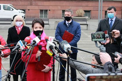 Briefing prasowy - mężczyzna i dwie kobiety stoją naprzeciwko ustawionych mikrofonów różnych redakcji radiowych i telewizyjnych 