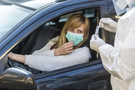 Pielęgniarz trzymający fiolkę, stoi obok siedzącej w samochodzie kobiety, w mobilnym punkcie wymazów