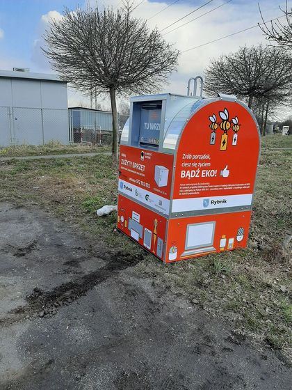 Czerwony kontener na odpady elektryczne, elektrośmieci, stojący na trawniku