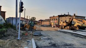 Droga w trakcie remontu, świeżo położony asfalt. Wzdłuż drogi domy, zieleń.