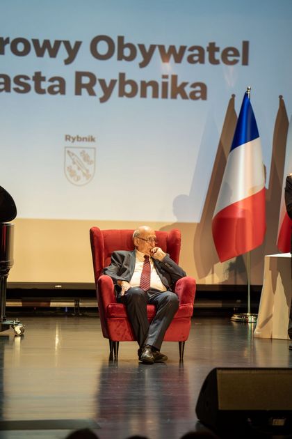 zdjęcie przedstawia honorowego obywatela miasta siedzącego na czerwonym fotelu