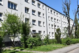 Jasny kilkupiętrowy budynek mieszkalny, na pierwszym planie zieleń, w tle błękitne niebo. 