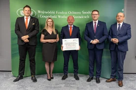 Grupa osób pozuje do zdjęcia. Jeden mężczyzna trzyma dyplom. 
