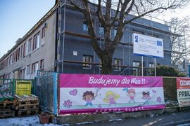 Budynek na terenie budowy. Z przodu baner z napisem „Budujemy dla Was! Budowa żłobka."