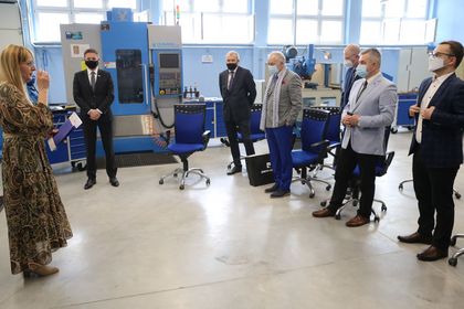 Grupa osób stojących w nowocześnie wyposażonej pracowni kształcenia zawodowego 