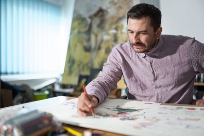 Mężczyzna szkicujący na kartce, siedzący przy biurku.