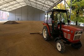 Budowa zadaszonego boiska - czerwony traktor na rozplantowanej ziemi pod zadaszeniem. 
