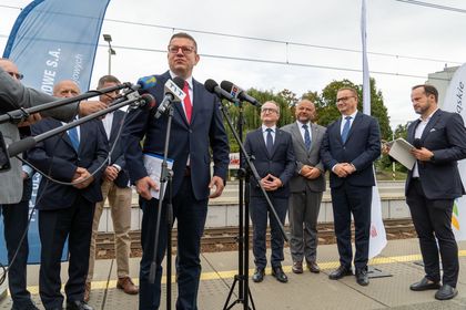 Zdjęcie przedstawia grupę mężczyzn stojących przy mikrofonach na peronie pkp. Jeden z mężczyzn mówi do mikrofonu.