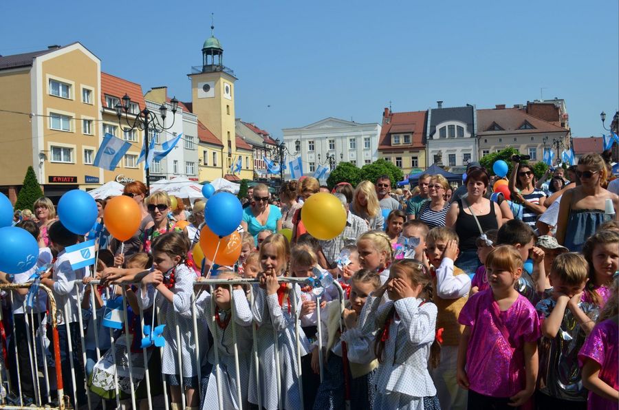 Tłum świętujących ludzi z balonami. W tle miejskie kamienice i błękitne niebo. 