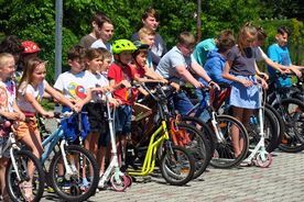 Grupa uczniów na rowerach i hulajnogach na placu szkolnym