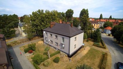 Blok mieszkalny w jasnych barwach, w tle zieleń, niebo i inne zabudowania
