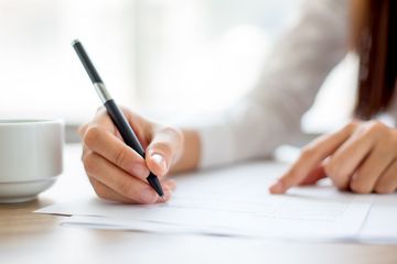 Ręka osoby piszącej na papierze lub podpisującej umowę przy stole w biurze