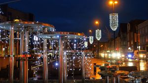 Wieczór. Świątecznie udekorowane miasto - lampki nad ulicami, choinki, i inne ozdoby.