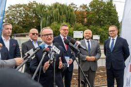 Zdjęcie przedstawia grupę mężczyzn stojących przy mikrofonach na peronie pkp. Jeden z mężczyzn mówi do mikrofonu.