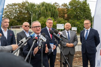 Zdjęcie przedstawia grupę mężczyzn stojących przy mikrofonach na peronie pkp. Jeden z mężczyzn mówi do mikrofonu.