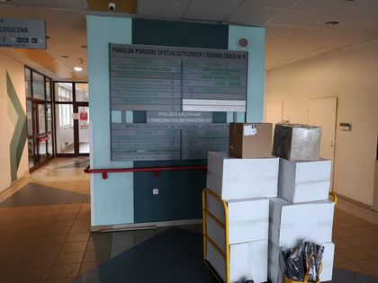 Paczki i kartony ustawione przed tablicą informacyjną szpitala