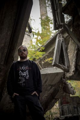 Mężczyzna w ciemnych okularach i ubraniu na tle postindustrialnych zabudowań