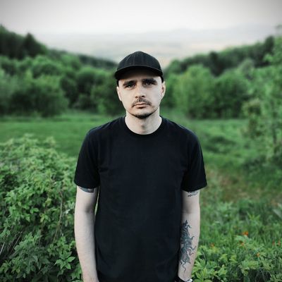 Mężczyzna w ciemnym ubraniu i czapce na tle zieleni