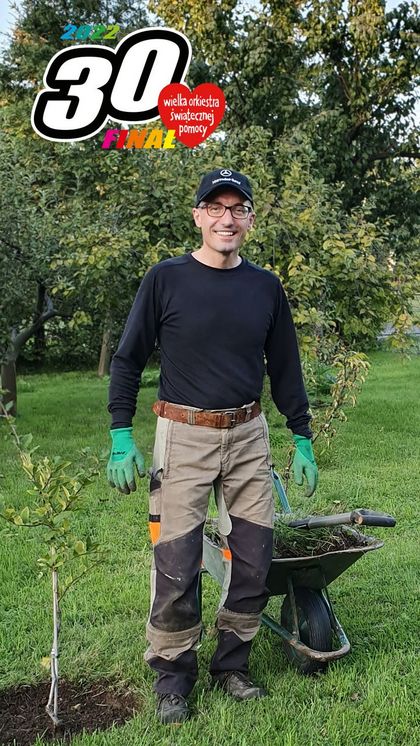 Prezydent Rybnika Piotr Kuczera w ogrodzie, w roboczym stroju. Za nim taczka i logo Wielkiej Orkiestry Świąteczenej Pomocy