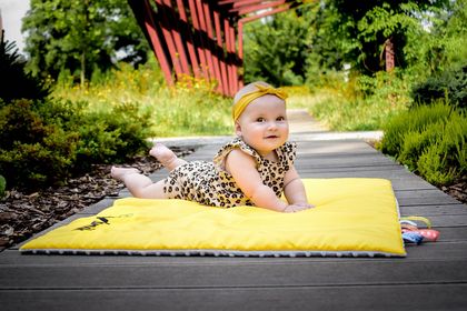 Kilkumiesięczna dziewczynka w body w panterkę na żółtym kocyku. W tle zieleń. 