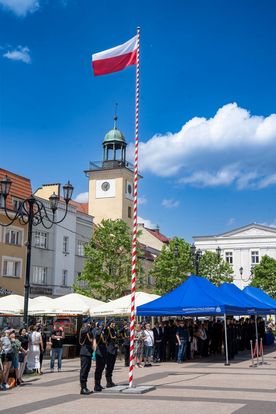 Zdjęcie przedstawia trzech mężczyzn w strojach strażackim salutujących do wywieszonej flagi polski. W tle ludzie.