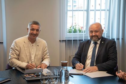 Zdjęcie przedstawia dwóch mężczyzn przy stole na oficjalnym spotkaniu.