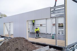 Zdjęcie przedstawia plac budowy. Wewnątrz konstrukcji budynku znajduje się dwóch mężczyzn.