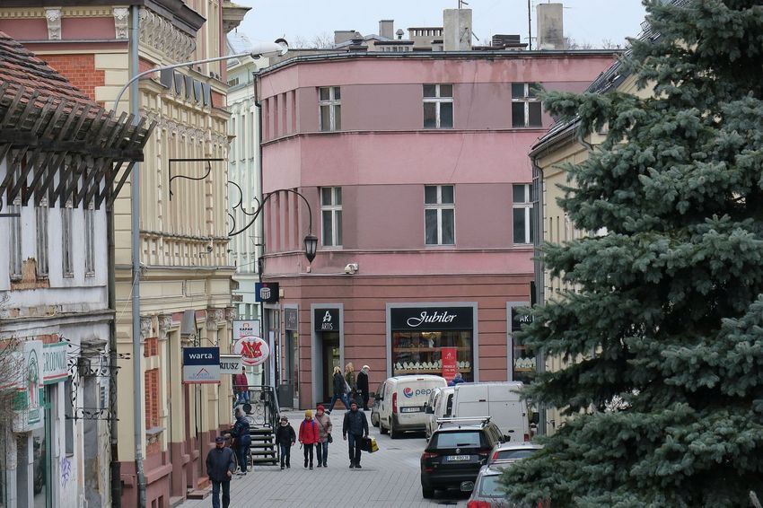 Kamienice w zabudowie śródmiejskiej. Deptak, na nim przechodnie i stojące samochody