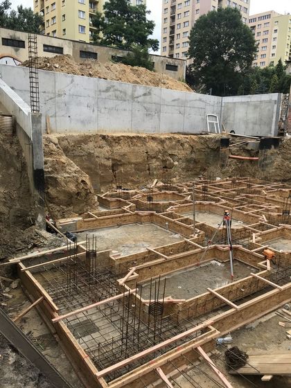 Budowa budynku - widoczne fundamenty oraz fragmenty konstrukcji betonowej i żelaznej. W tle osiedle bloków mieszkalnych. 