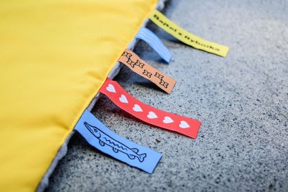 5 wszytych w krawędź żółtego kocyka kolorowych żakardowych tkanych metek. 