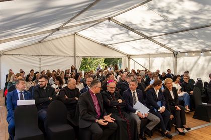 Na zdjęciu widać grupę ludzi siedzących w pomieszczeniu na oficjalnym wydarzeniu.