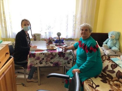 Dwie kobiety - starsza i młodsza w pokoju Miejskiego Domu Pomocy Społecznej siedzą przy stole. 
