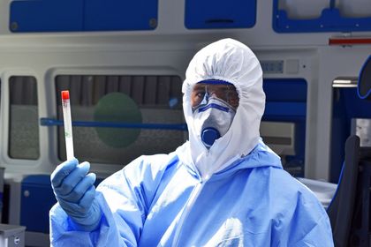 Wymazobus fot.K 3 Medyk w kombinezonie ochronnym. W zabezpieczonej rękawiczką ręką fiolka z preparatem do badania.