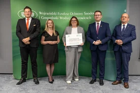 Grupa osób pozuje do zdjęcia. Jedna z kobiet trzyma dyplom.