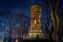Nocne zdjęcie zabytkowej, ceglanej wieży ciśnień otoczonej parkiem