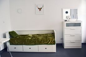 Jasne wnętrze, białe łóżko z zielona kapą, biała szafka