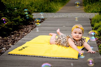 Kilkumiesięczna dziewczynka w body w panterkę na żółtym kocyku. Obok bańki mydlane. W tle zieleń. 