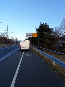 Tablica ostrzegawcza i informacyjna na ulicy. Obok biały samochód.