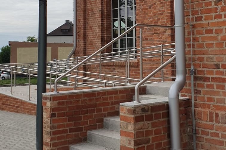Ignacy 05 2020 17 Wejście do budynku z czerwonej cegły. Otaśmowany podjazd dla osób niepełnosprawnych.